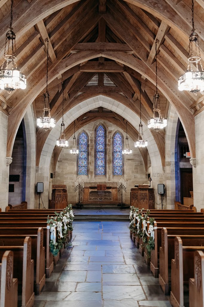 Duncan Memorial Chapel wedding interior with wooden pews, stained glass windows, and floral aisle decorations.