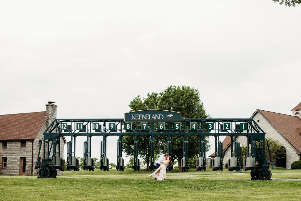 Engaged couple kissing in front of the Keeneland starting gates.