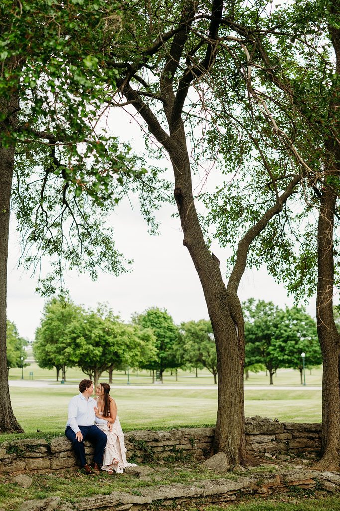 Engaged couple sitting together beneath large trees during their Keeneland engagement session.