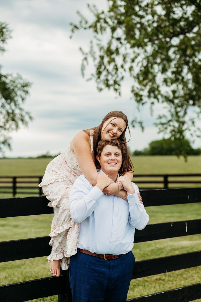 Playful engaged couple smiling together beside a black fence.