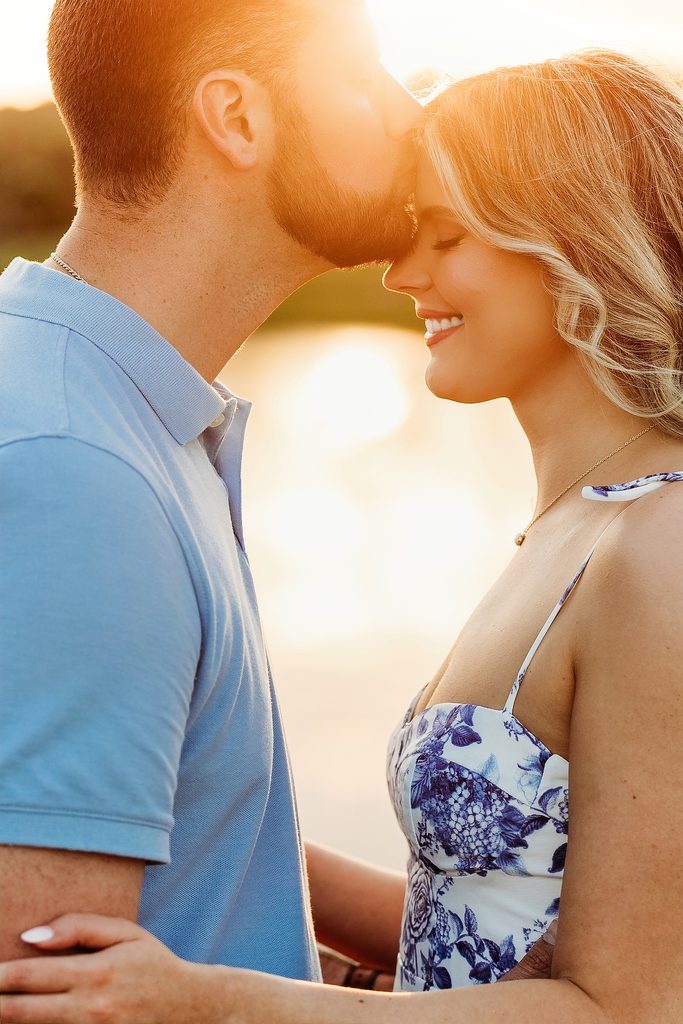 Engaged couple sharing a forehead kiss in warm golden hour light.
