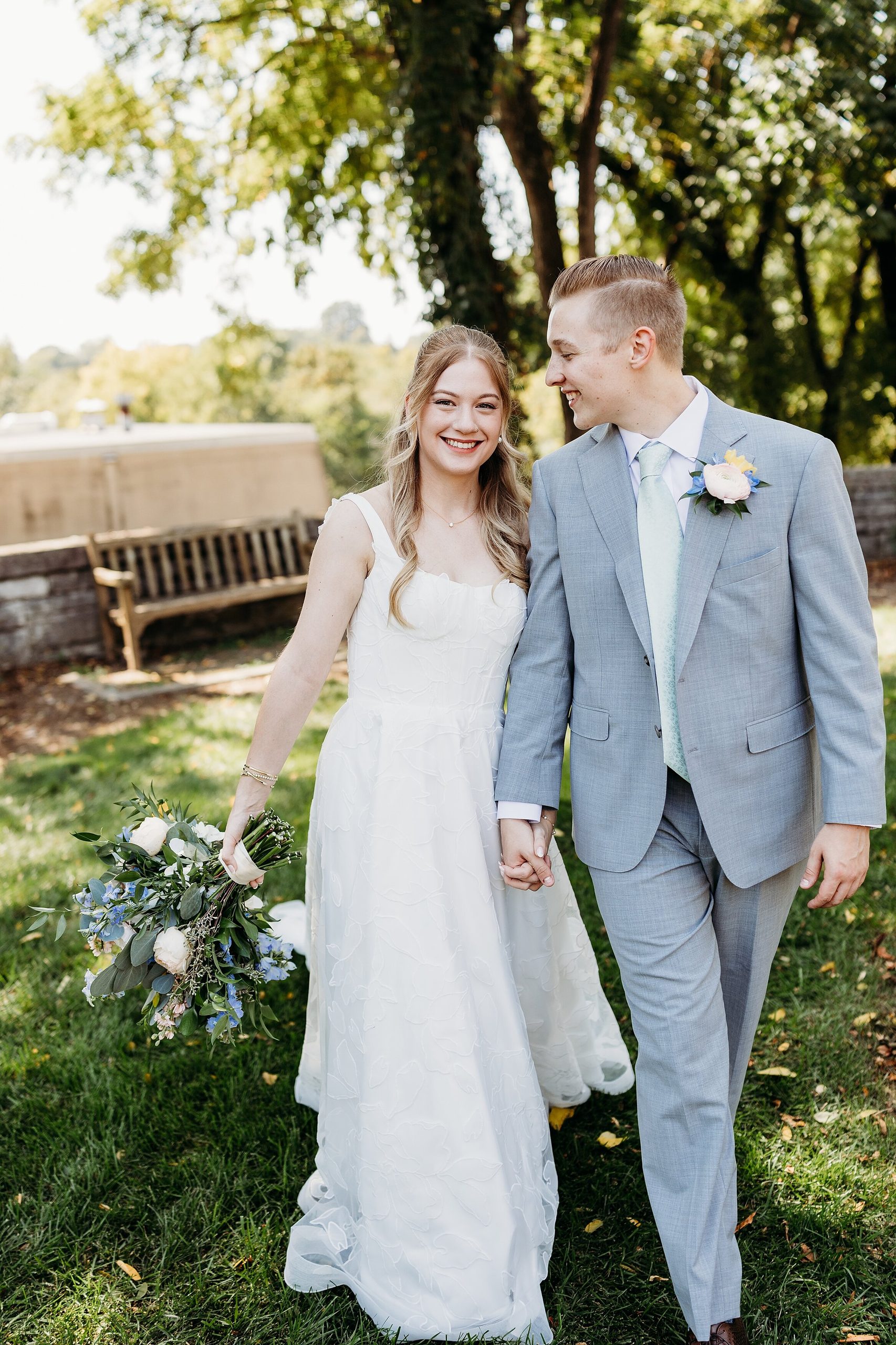 Groom looking at bride while walking hand in hand through gardens