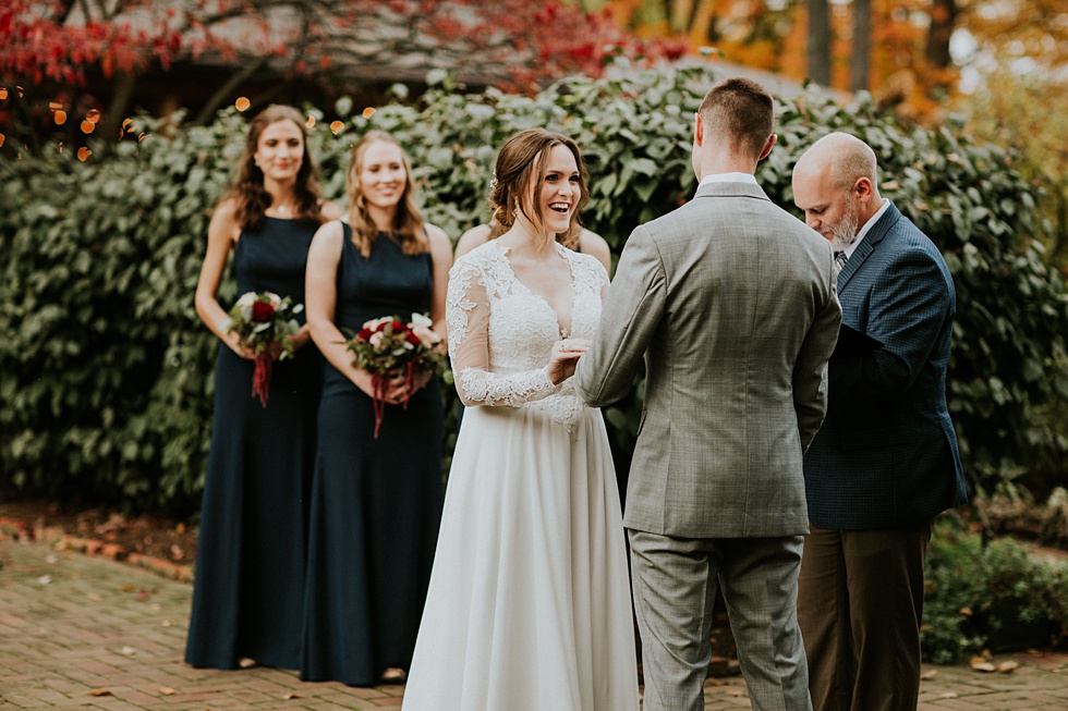 Bride smiles at the groom while exchanging vows during an autumn garden wedding ceremony.