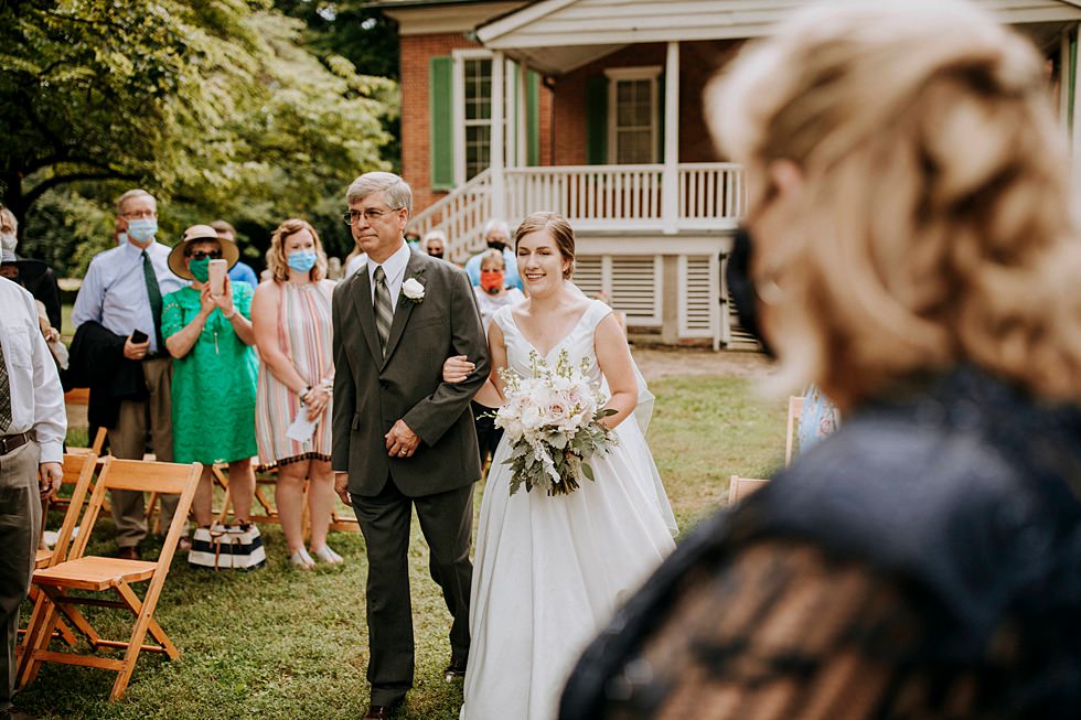 Bride walks down the aisle with her father during an outdoor wedding ceremony.
