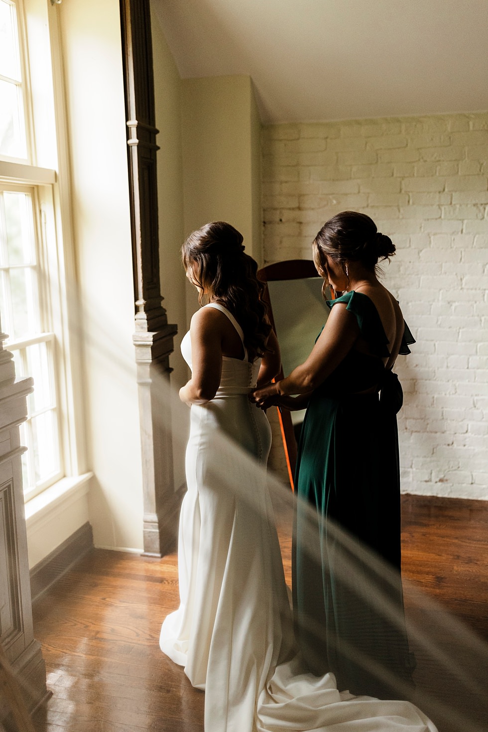 Bride getting ready with bridesmaid in front of window