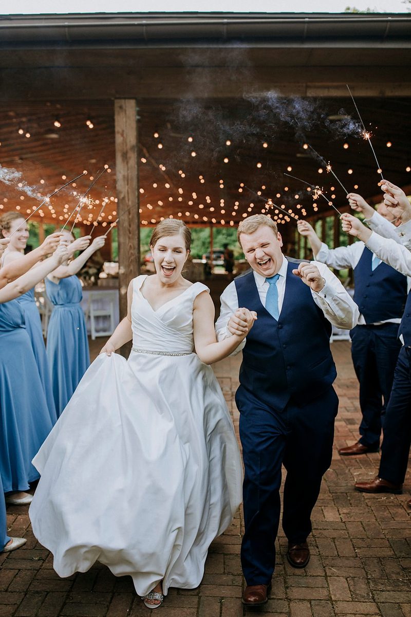 Bride and groom laugh while running through a sparkler exit with their wedding party.