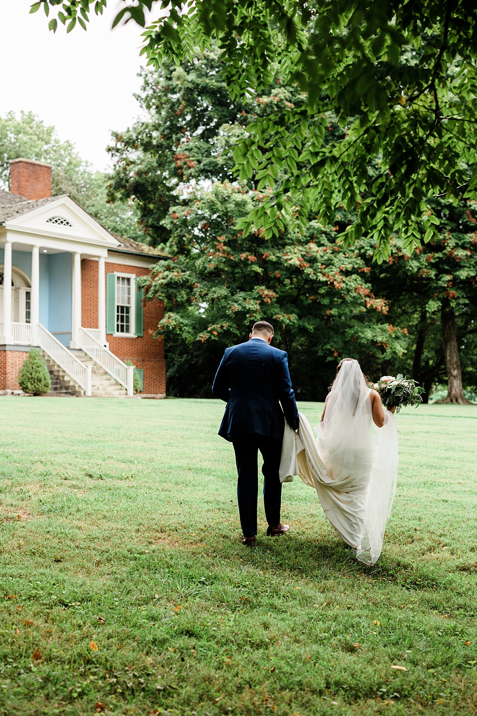 Bride and groom walk across the lawn toward Farmington historic house.